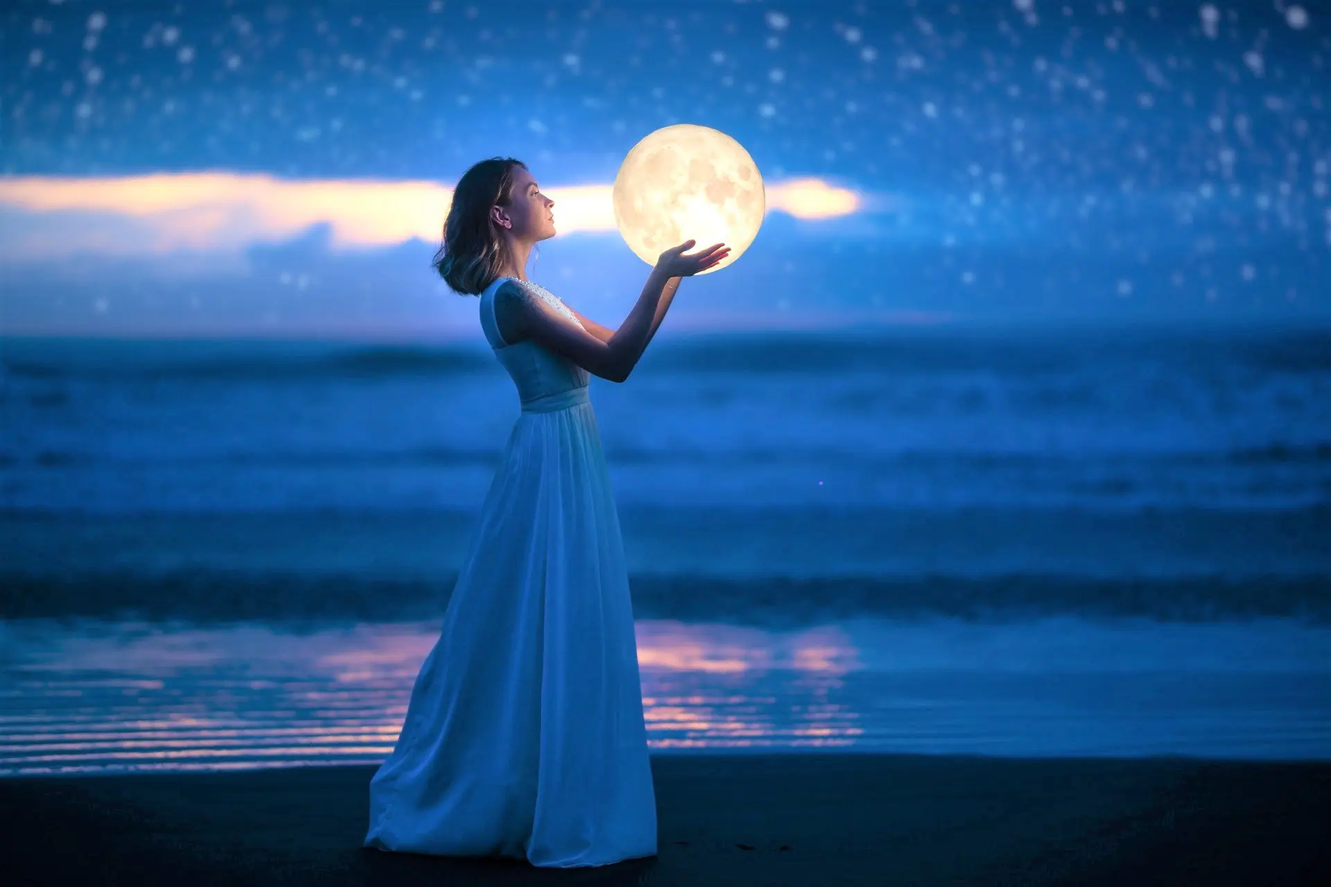 A young girl on a night beach holds the moon, with a starry sky